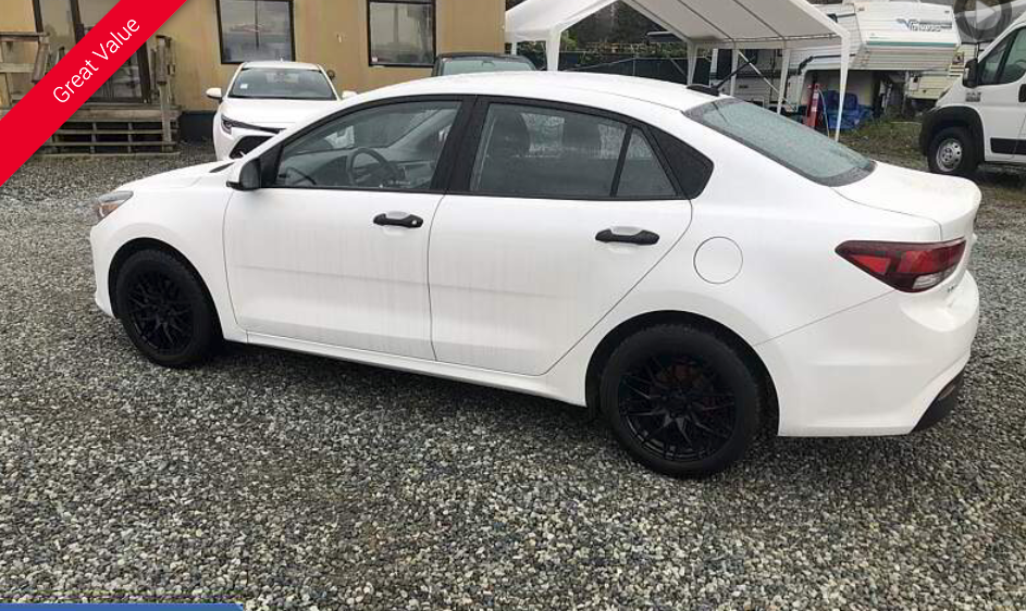 White sedan with black wheels parked outdoors on gravel.