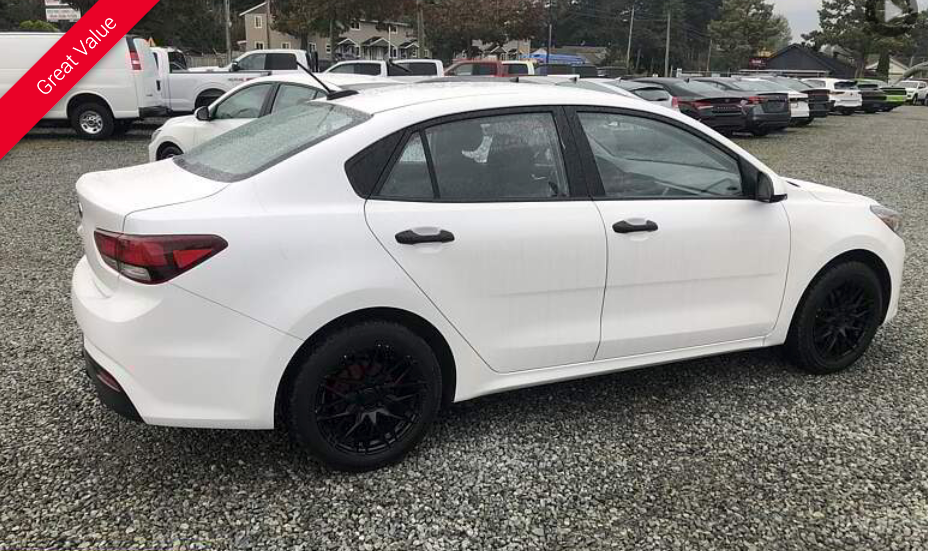 White sedan with black wheels parked on gravel lot.