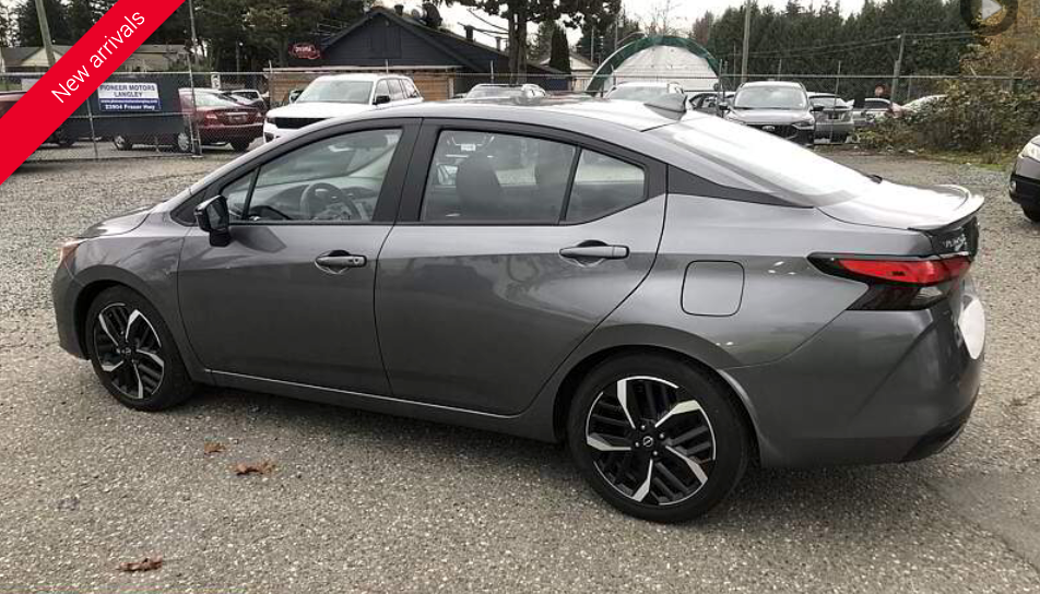 Gray Nissan sedan parked on gravel lot. Black wheels, tinted windows, and red 