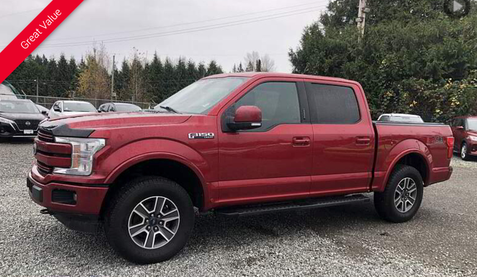 Red Ford F-150 pickup truck parked on gravel in front of a building on an overcast day.