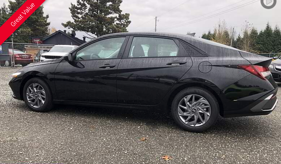 Black Hyundai Elantra sedan parked on a gravel lot near a building and trees.