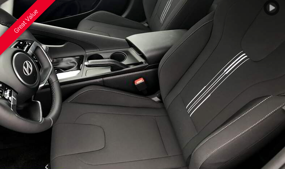 Black car interior, driver's seat, console with cup holders, white stitching, steering wheel visible.