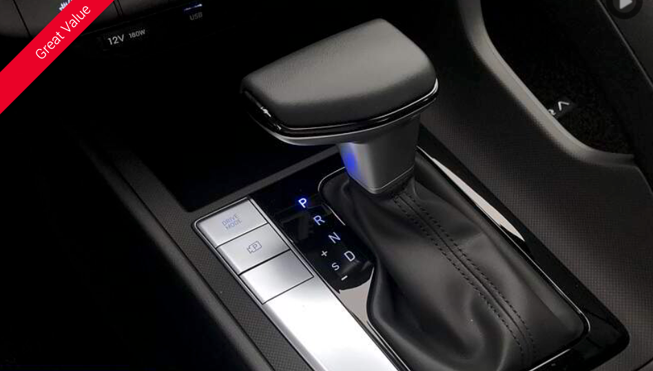 Close-up of a car's gear shift lever, center console with buttons, and surrounding black interior.