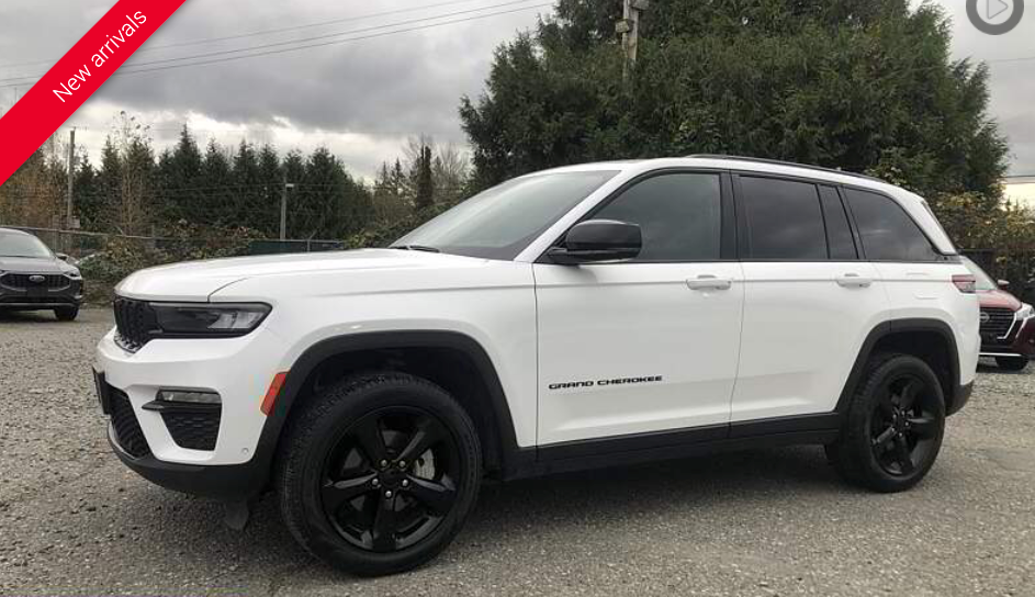 White Jeep Grand Cherokee SUV with black wheels, parked outdoors on gravel.