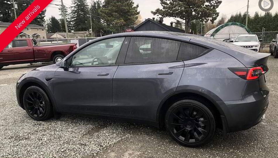 Gray Tesla Model Y with black wheels parked outside.