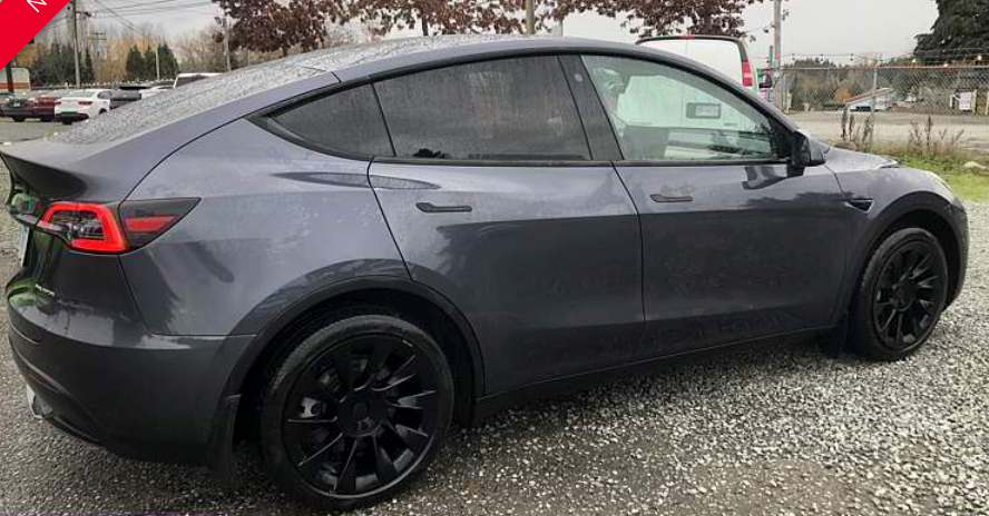 Gray Tesla Model Y parked outdoors with black wheels and tinted windows.
