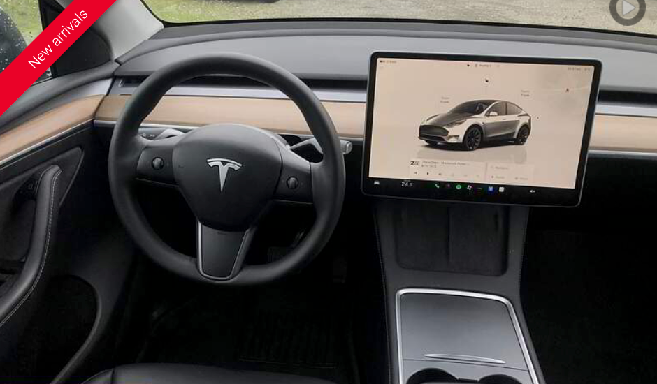 Interior of a Tesla car, black interior, steering wheel, large central screen, and console.