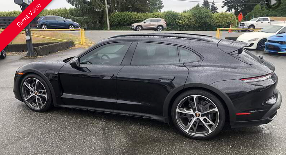 Black Porsche Taycan Cross Turismo parked on a wet surface with other vehicles in background.