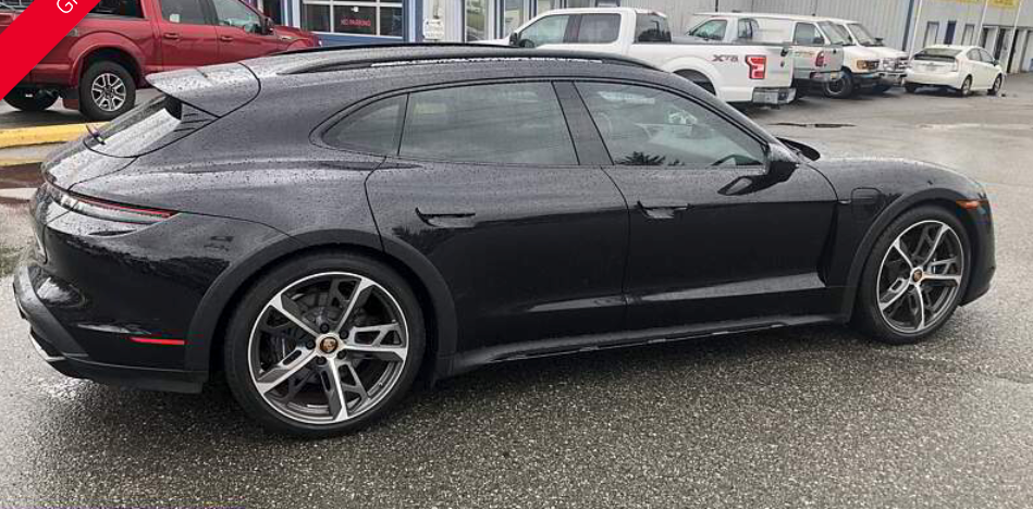 Black Porsche Taycan Cross Turismo parked on wet pavement near other vehicles.