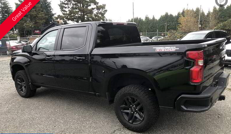 Black Chevrolet Silverado truck, parked on gravel lot.