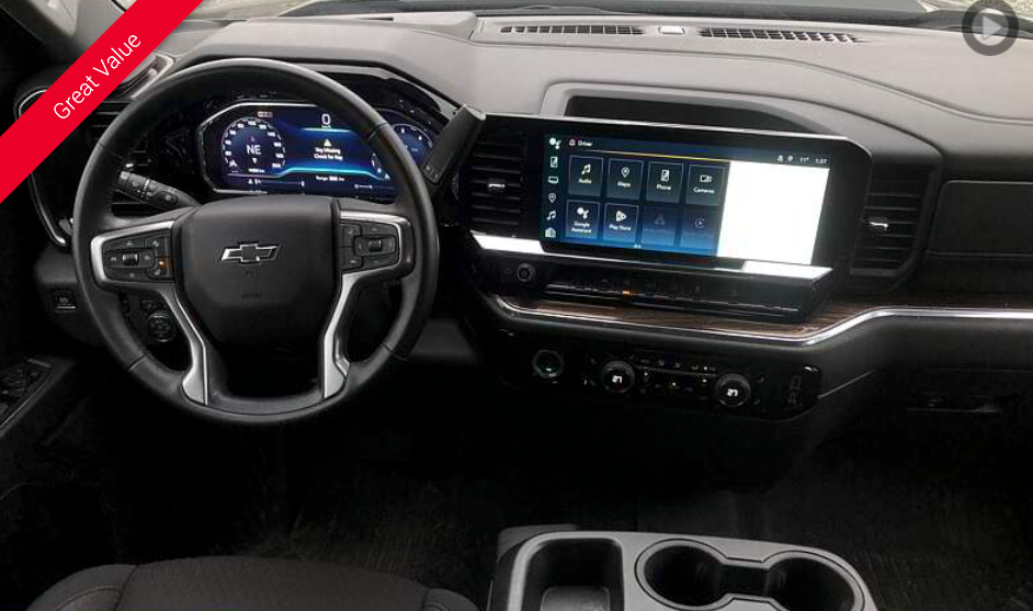 Dashboard of a Chevrolet truck, showing the steering wheel, infotainment screen, and cup holders. Black and silver interior.