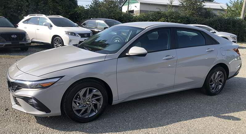 Gray Hyundai Elantra sedan parked on gravel lot with other vehicles in the background.
