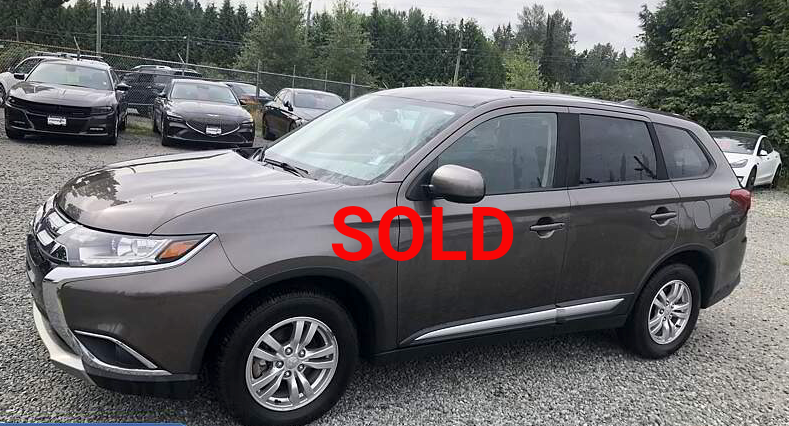 Brown Mitsubishi Outlander SUV parked in a lot with other vehicles and trees in the background.