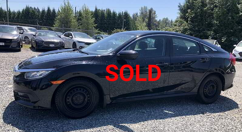 Black Honda Civic sedan parked outdoors on gravel, other cars in the background on a sunny day.