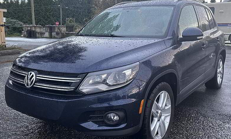 Dark blue Volkswagen Tiguan SUV parked outdoors, front view. Wet with rain.