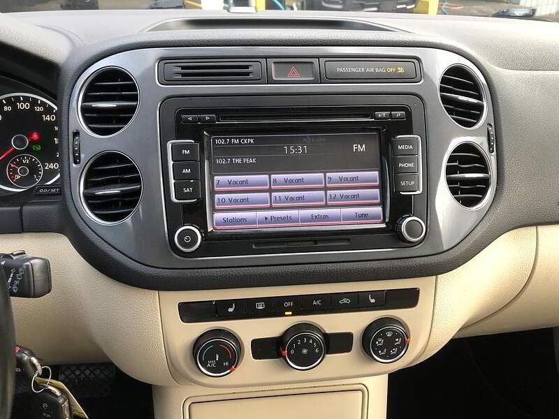 Car dashboard with radio display, vents, and climate controls. Beige and black interior.