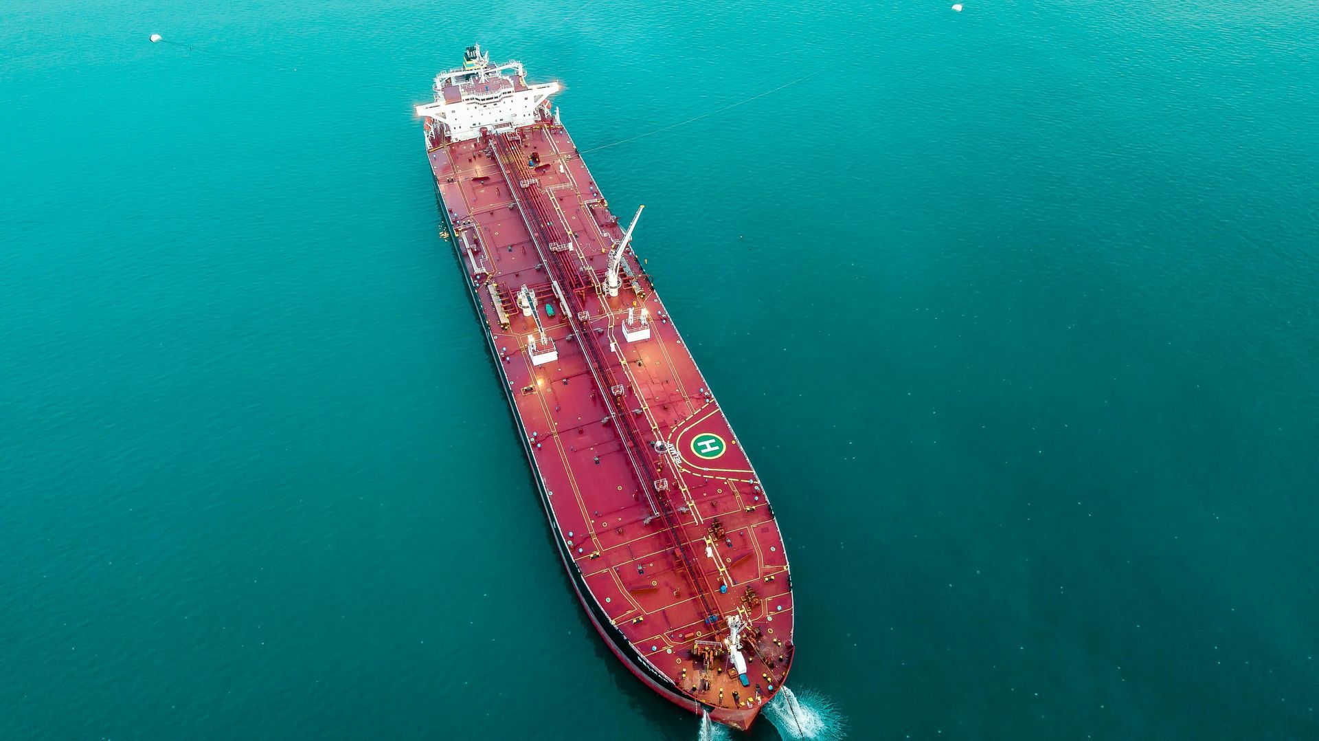 Aerial view of a large red oil tanker ship on teal-colored water.