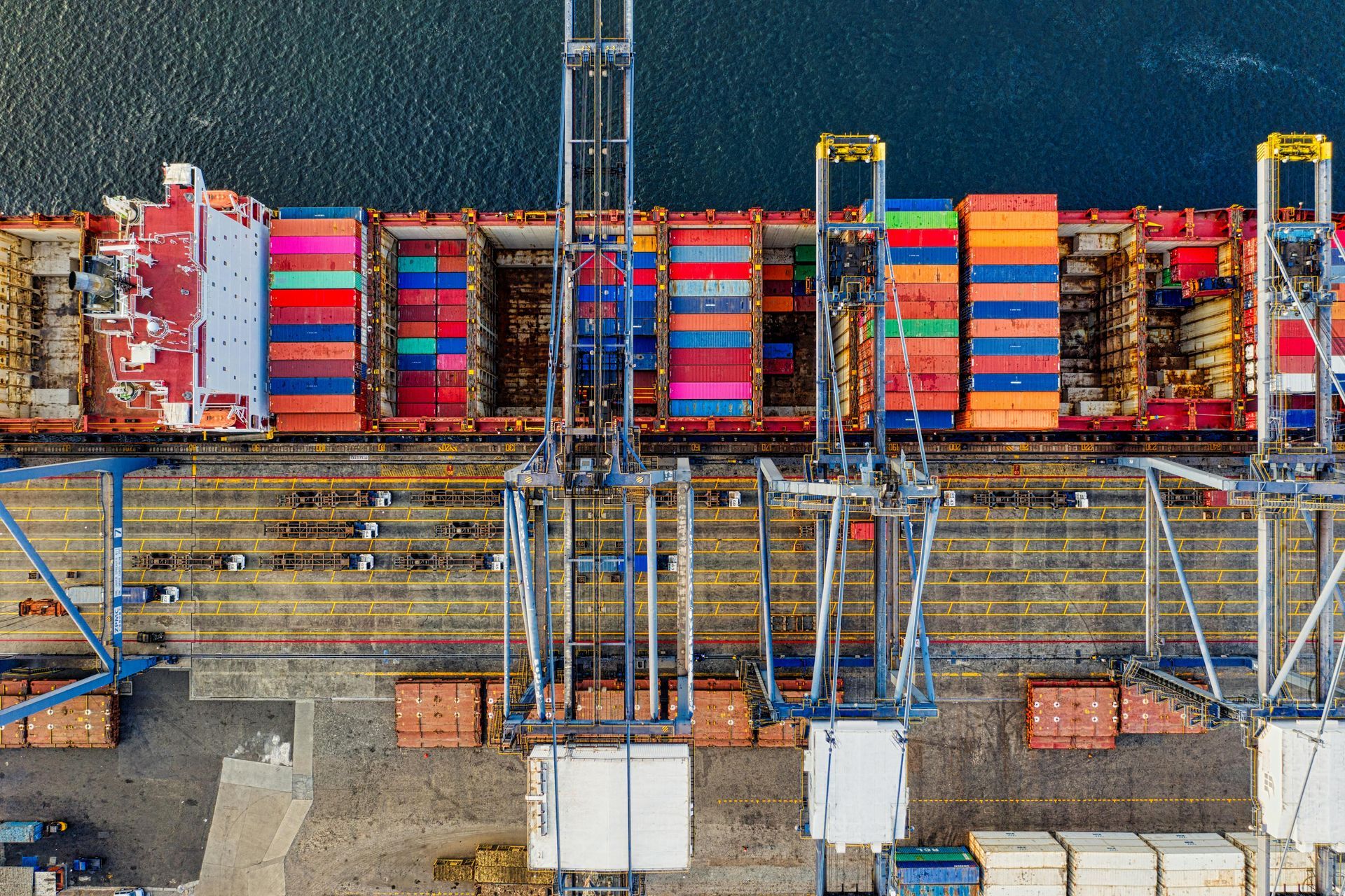 Overhead view of a cargo ship at a dock with colorful shipping containers being loaded.
