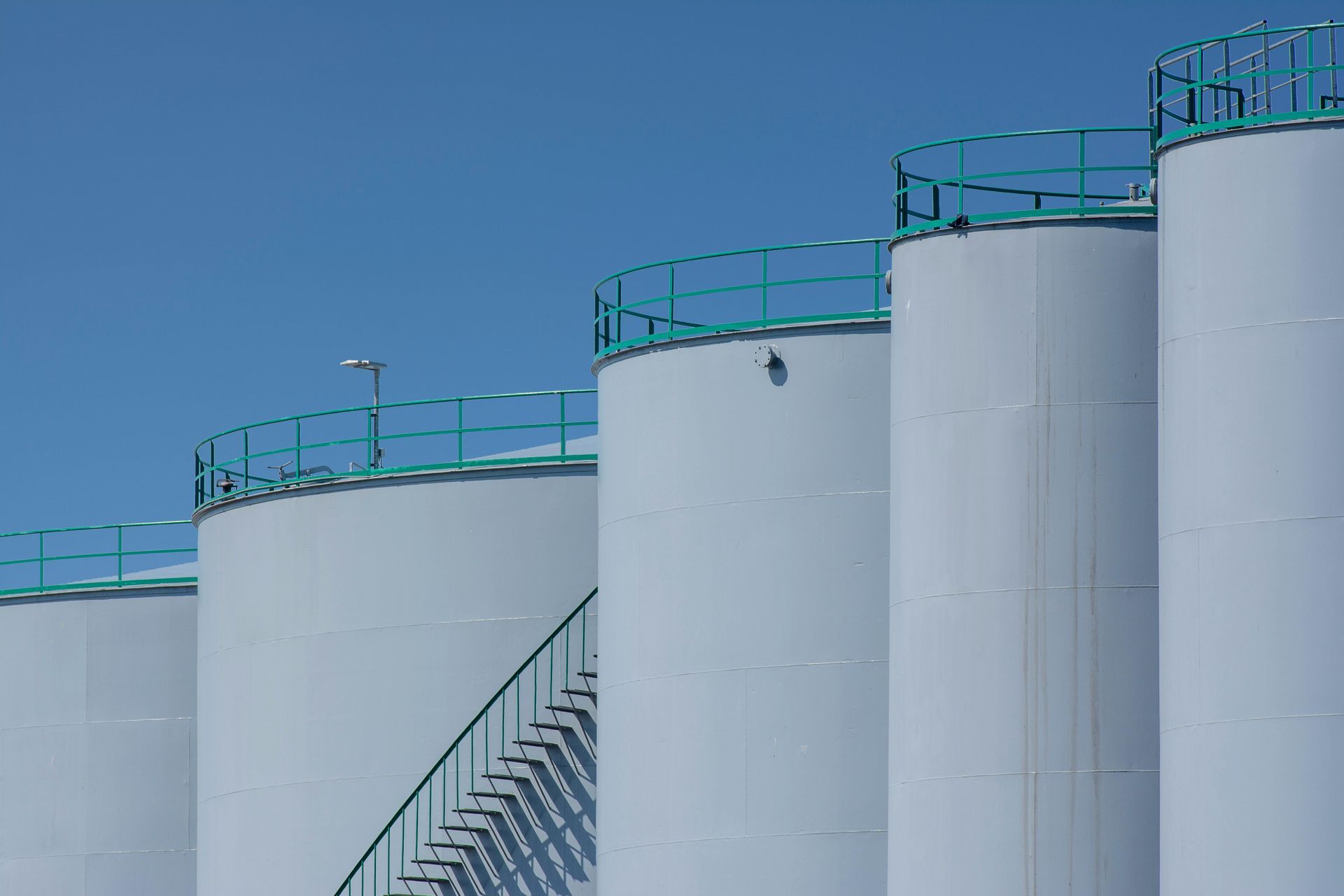 Tanker ship docked at a port next to industrial storage tanks and a bridge in the distance.