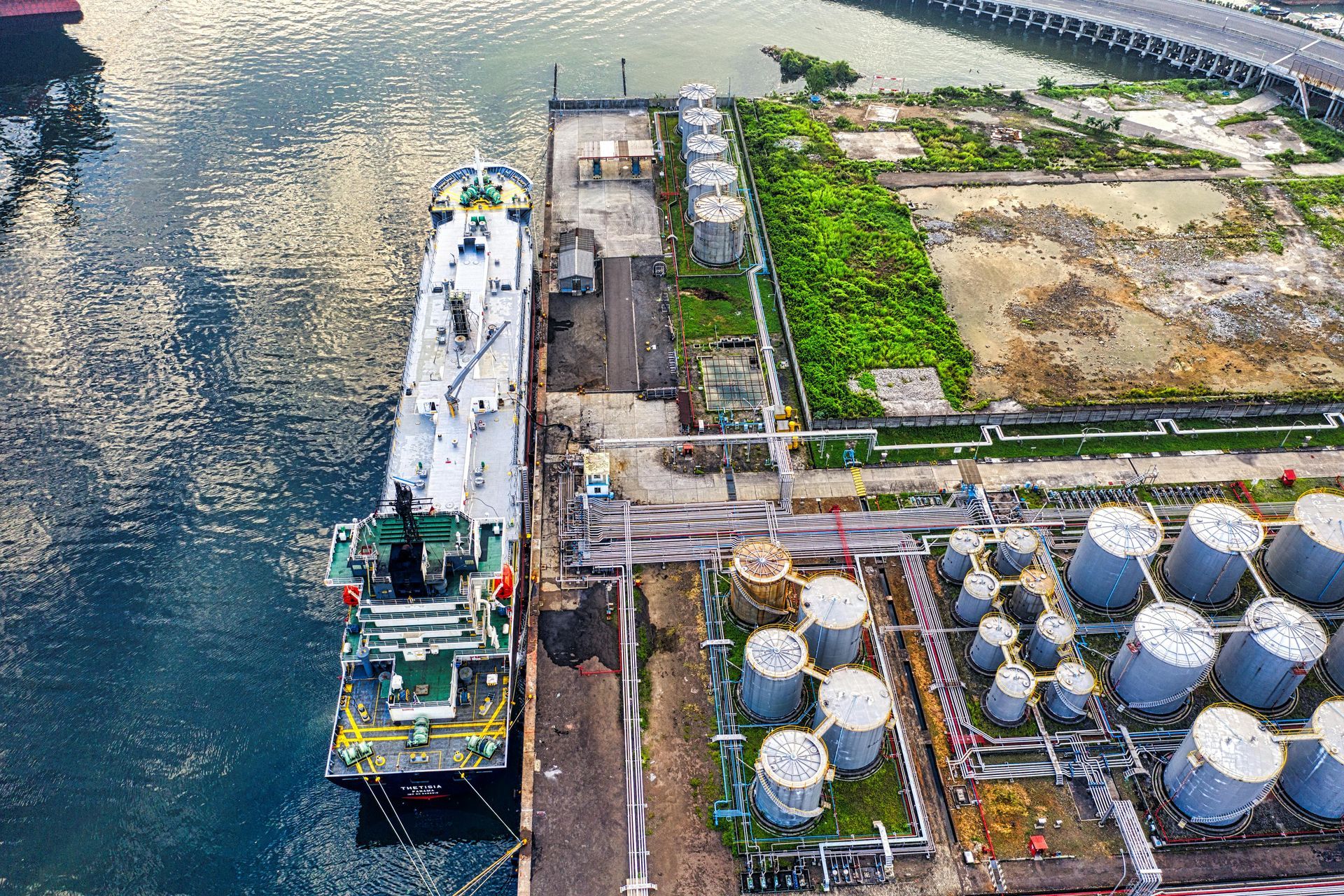Aerial view of a tanker docked at a port next to storage tanks. Water, industrial area.