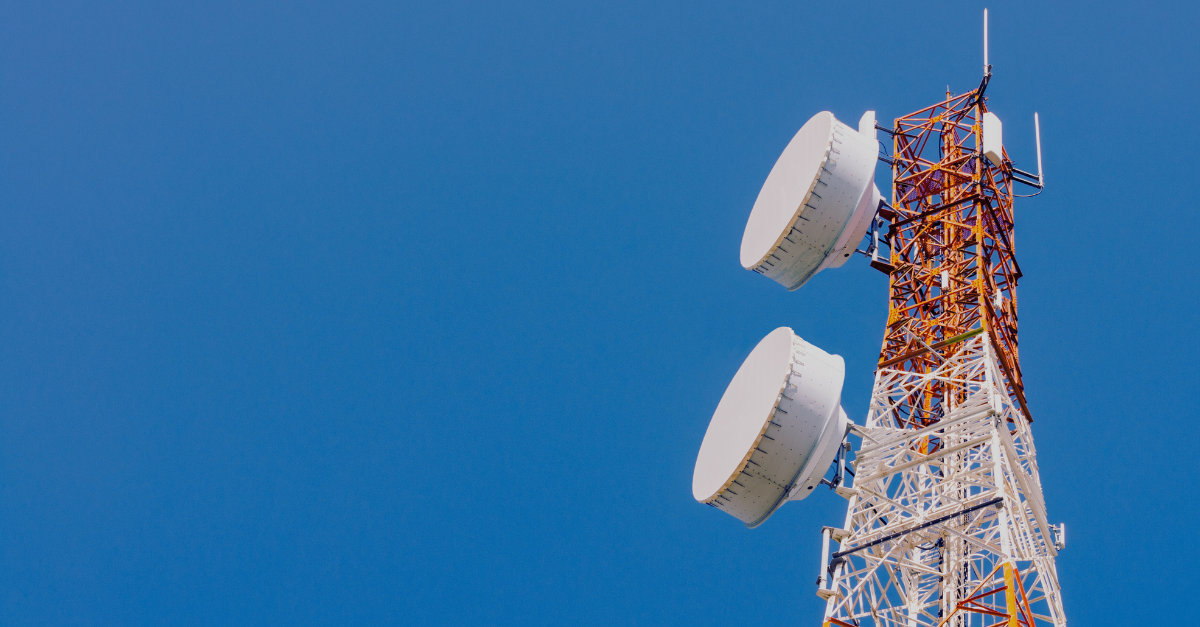 Telecommunication tower with large white antennas against a bright blue sky.