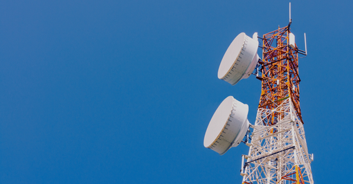 Telecommunication tower with large white antennas against a bright blue sky.