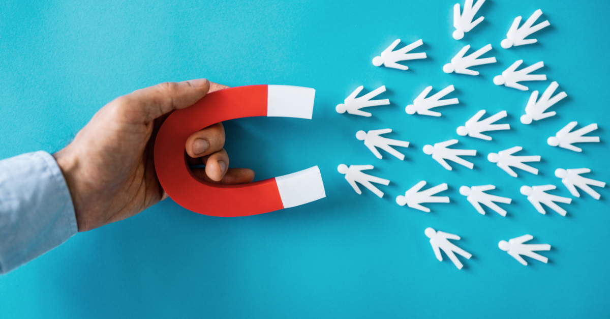 Hand holding a red horseshoe magnet attracting white paper cutouts of people on a blue background.