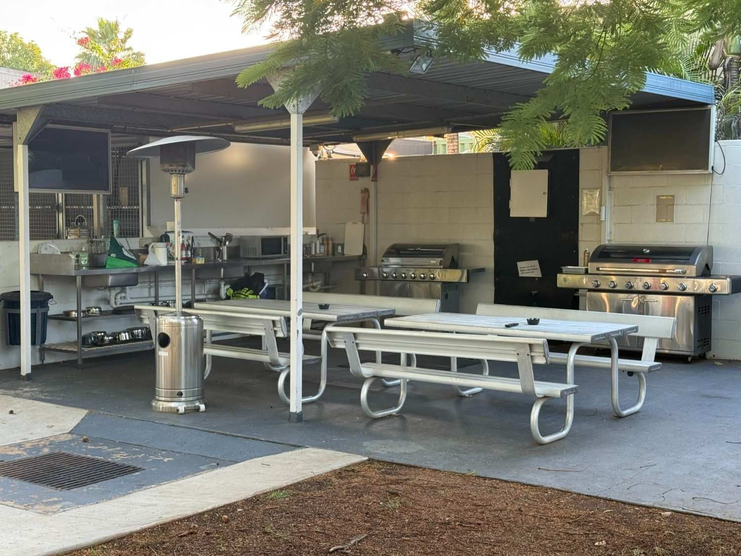 Outdoor Cooking Area with Picnic Tables, Grills, and A Metal Awning — Leichhardt Accommodation in Mornington, QLD
