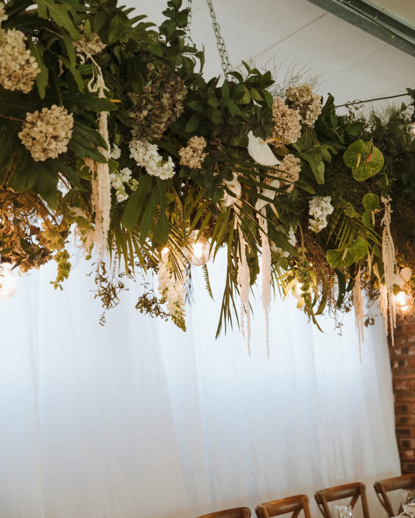 A wooden sign with flowers on it is sitting in front of a brick wall.