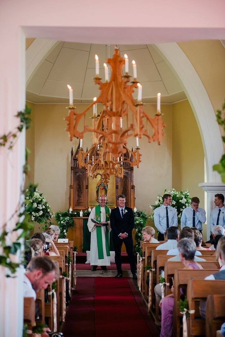 A bride and groom are getting married in a church with a chandelier hanging from the ceiling.