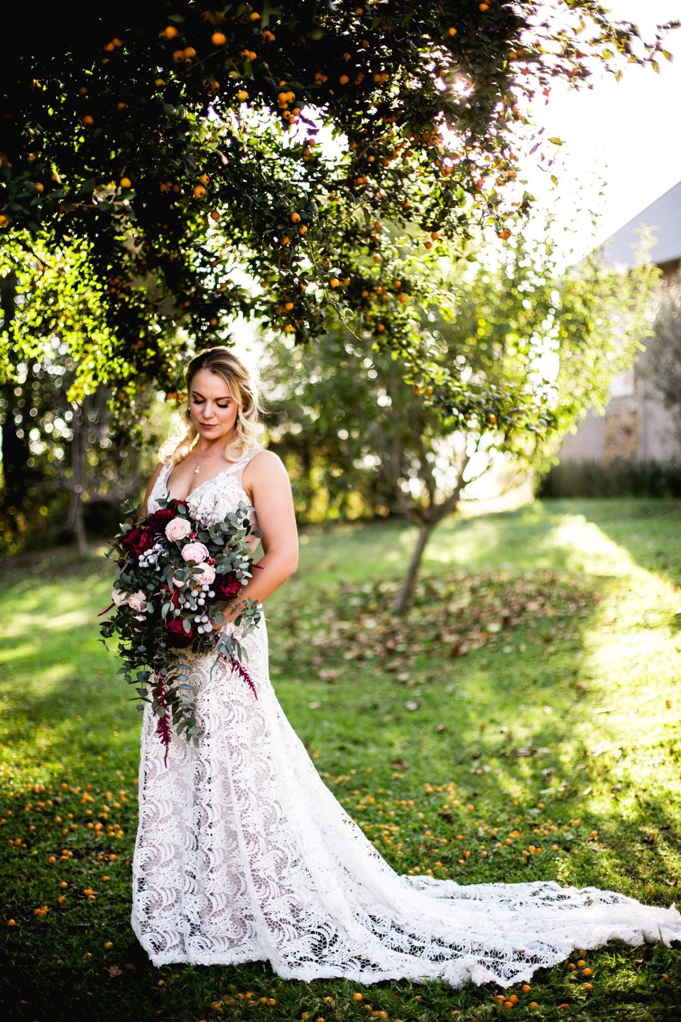 A bride in a lace wedding dress is holding a bouquet of flowers.