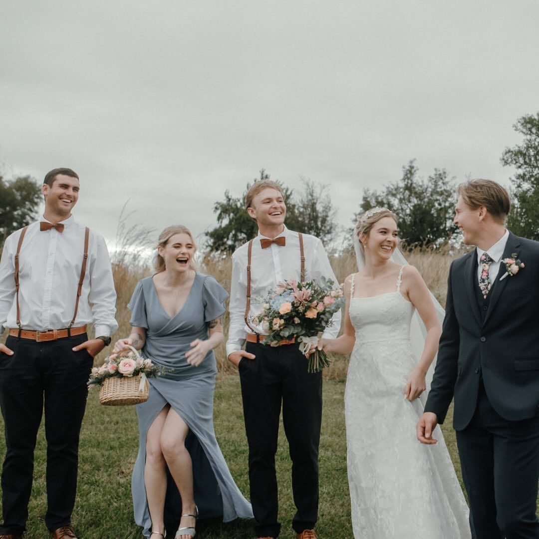 A bride and groom are walking with their wedding party in a field.