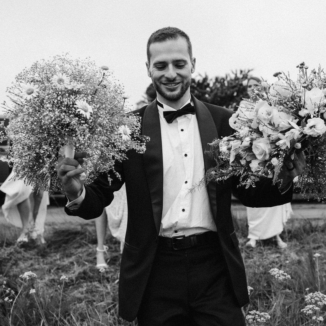 A man in a tuxedo is holding two bouquets of flowers.