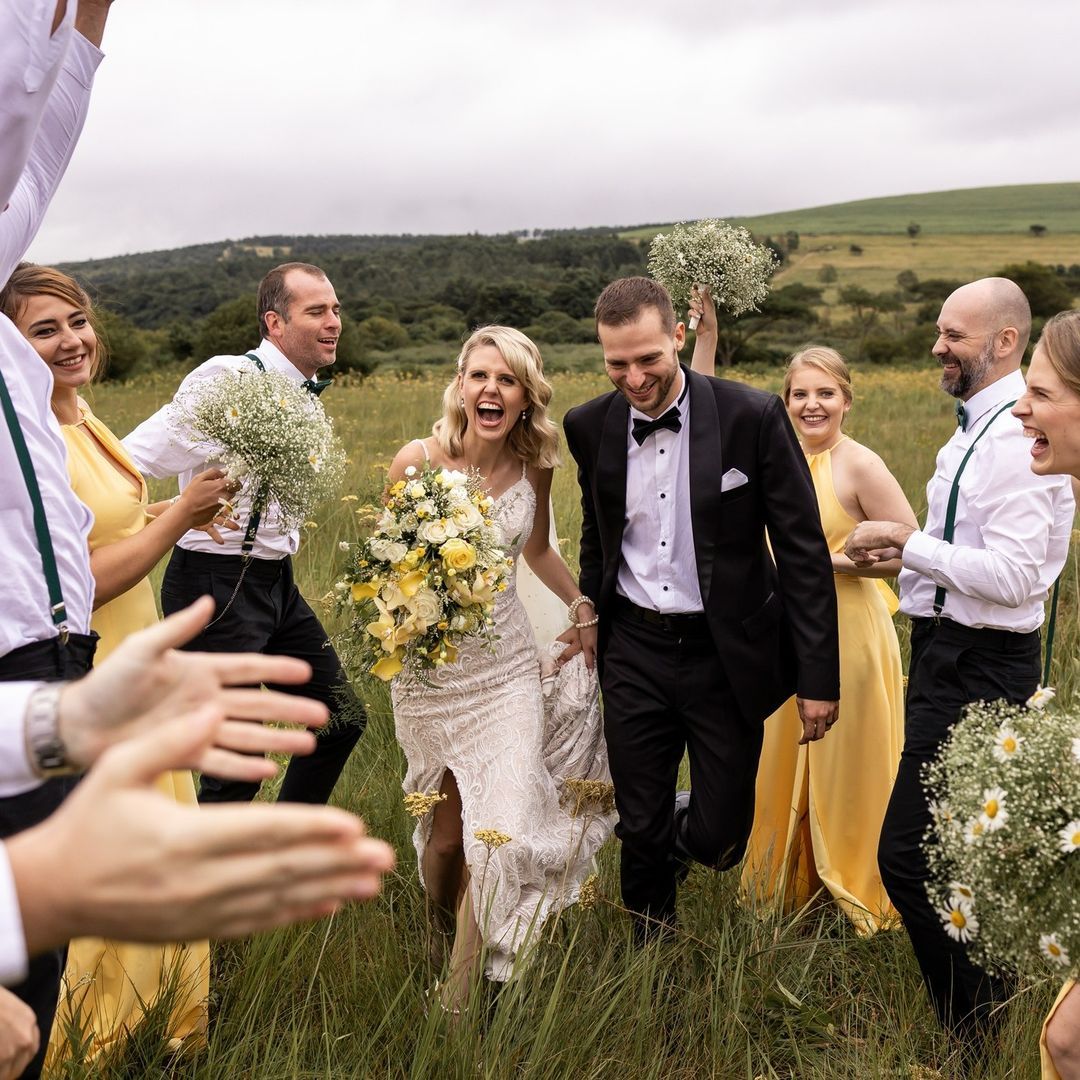 A bride and groom are walking through a field with their wedding party.