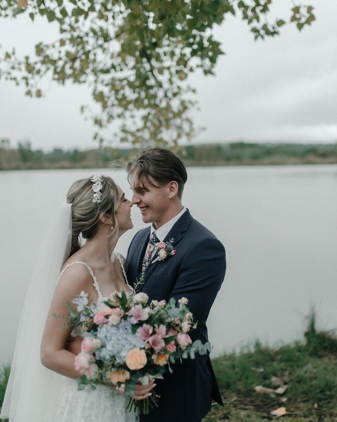 A bride and groom are kissing in front of a lake.