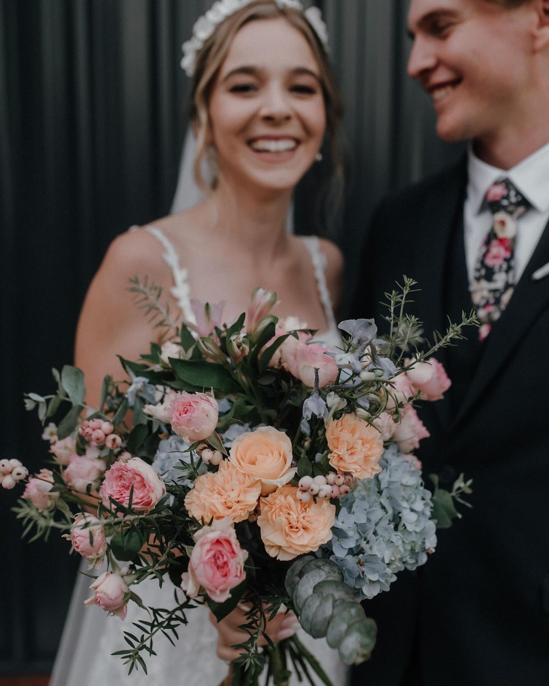 A bride and groom are posing for a picture and the bride is holding a bouquet of flowers.