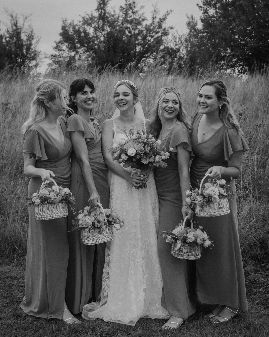 A bride and her bridesmaids are posing for a black and white photo in a field.