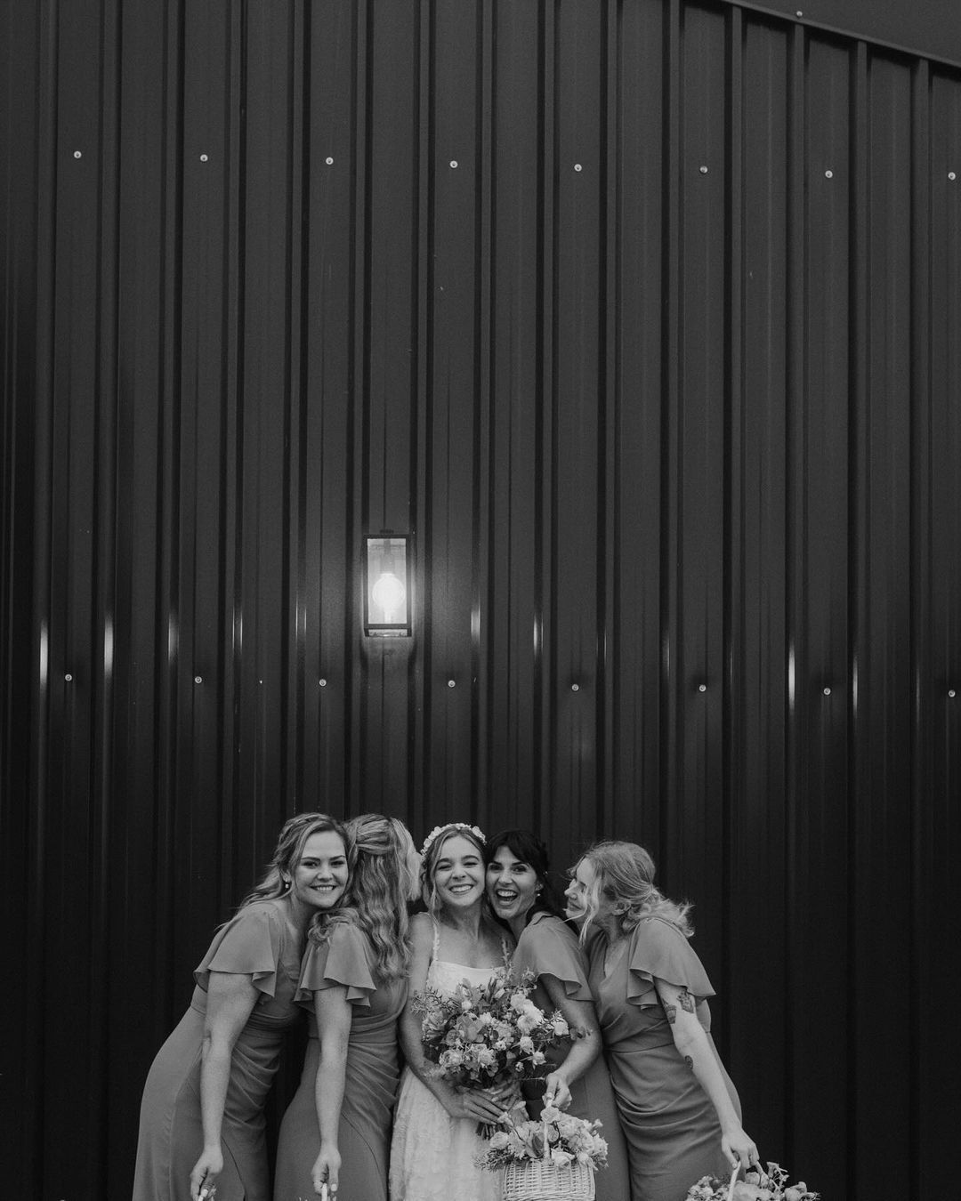 A bride and her bridesmaids are posing for a picture in front of a black wall.