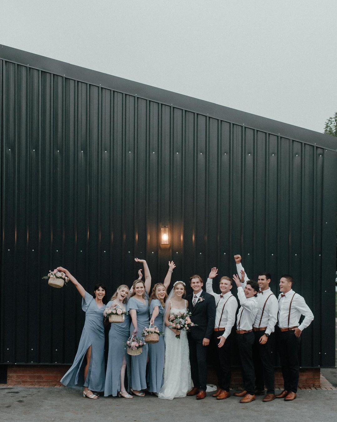 A bride and groom are posing for a picture with their wedding party in front of a building.