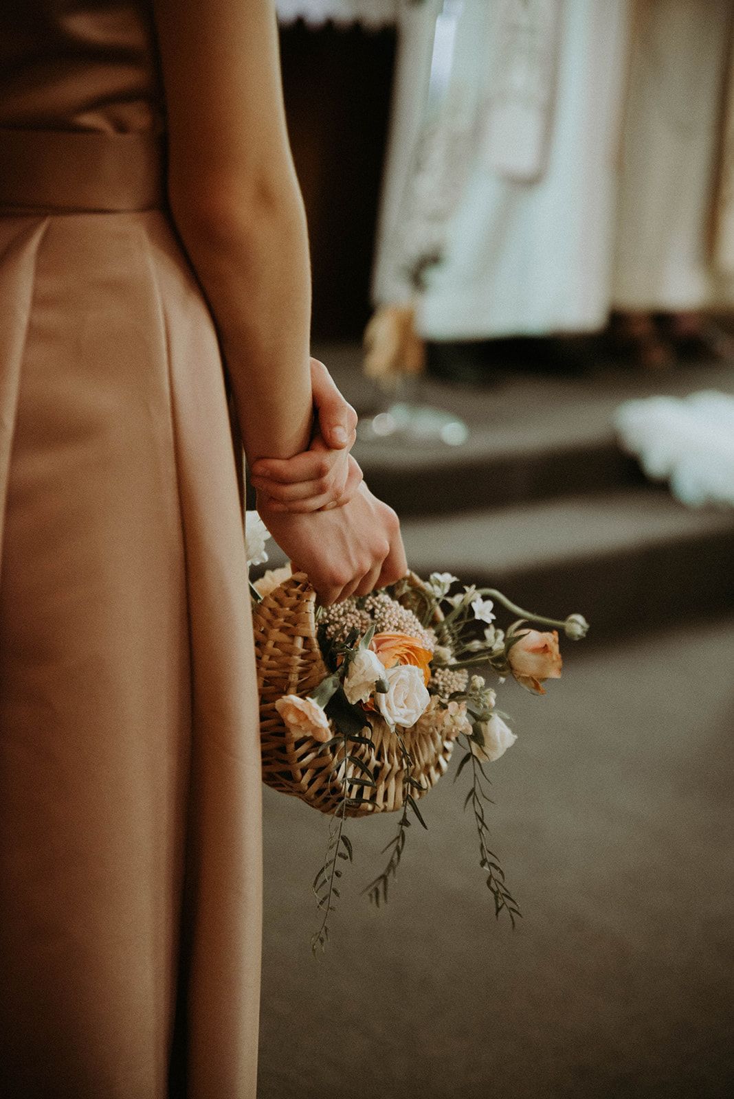 A bridesmaid is holding a basket of flowers in her hand.