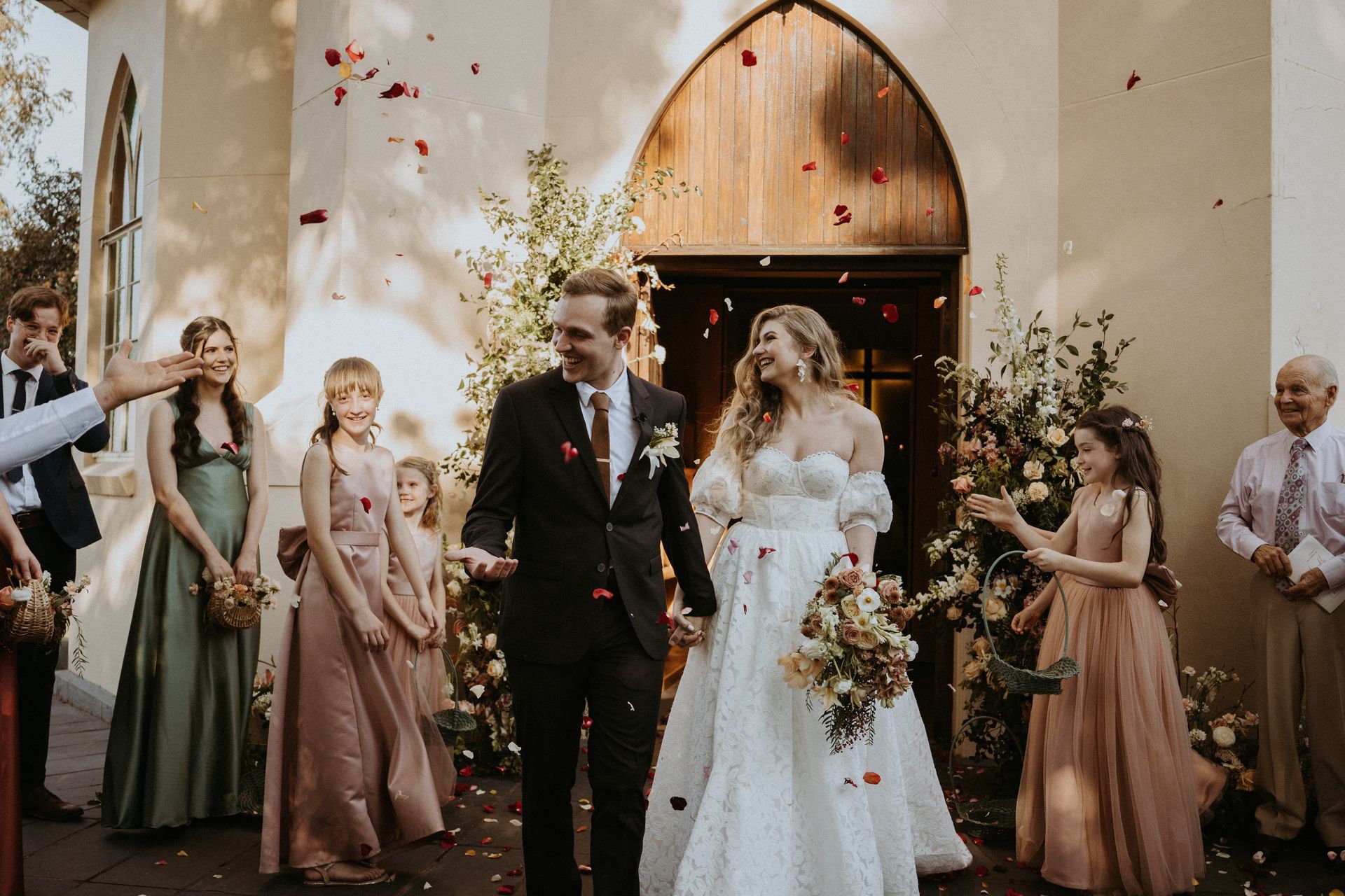 A bride and groom are walking out of a church with their wedding party.