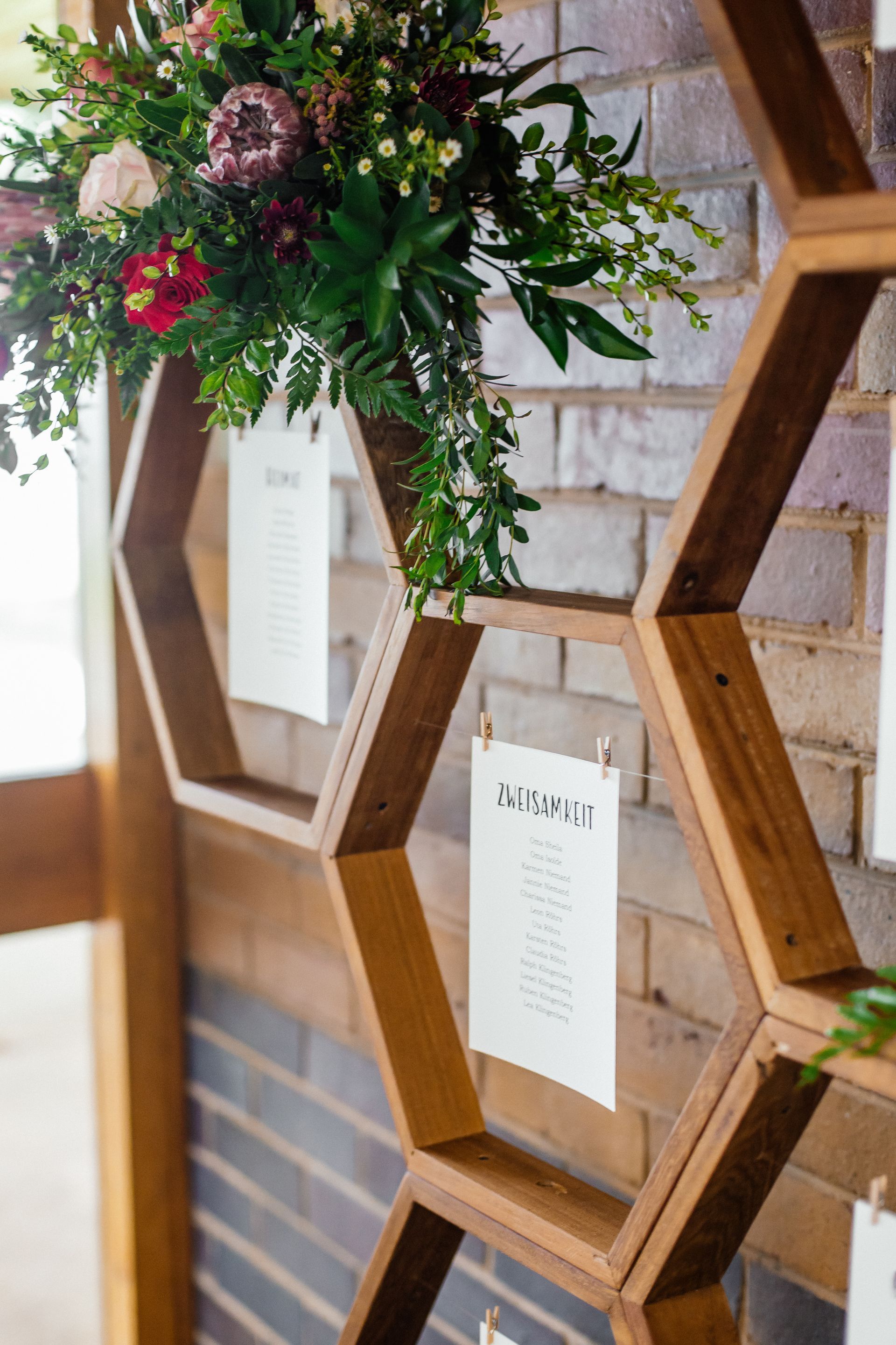 A wooden shelf with flowers on it is hanging on a brick wall.
