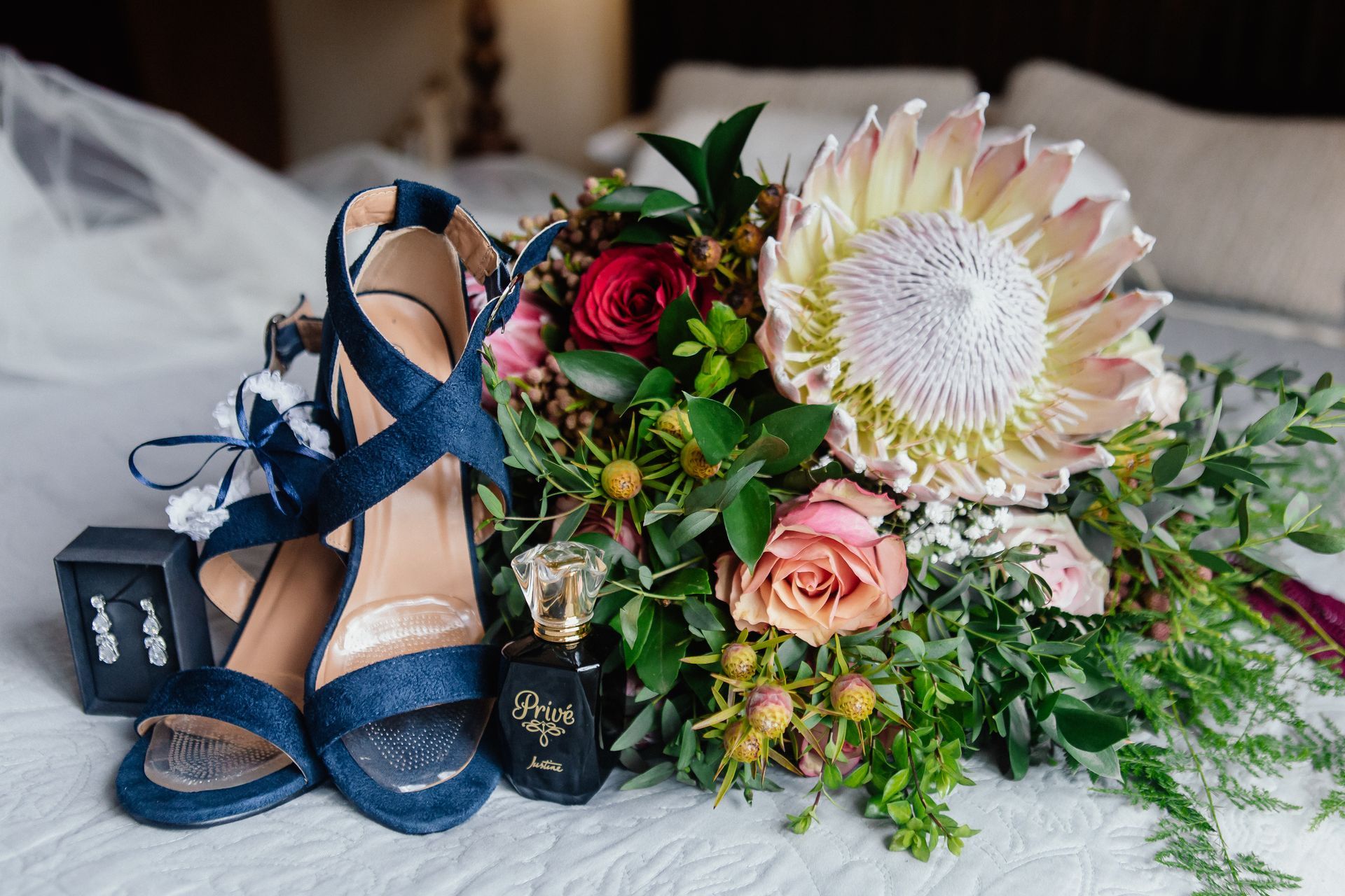 A bouquet of flowers and shoes are on a bed.