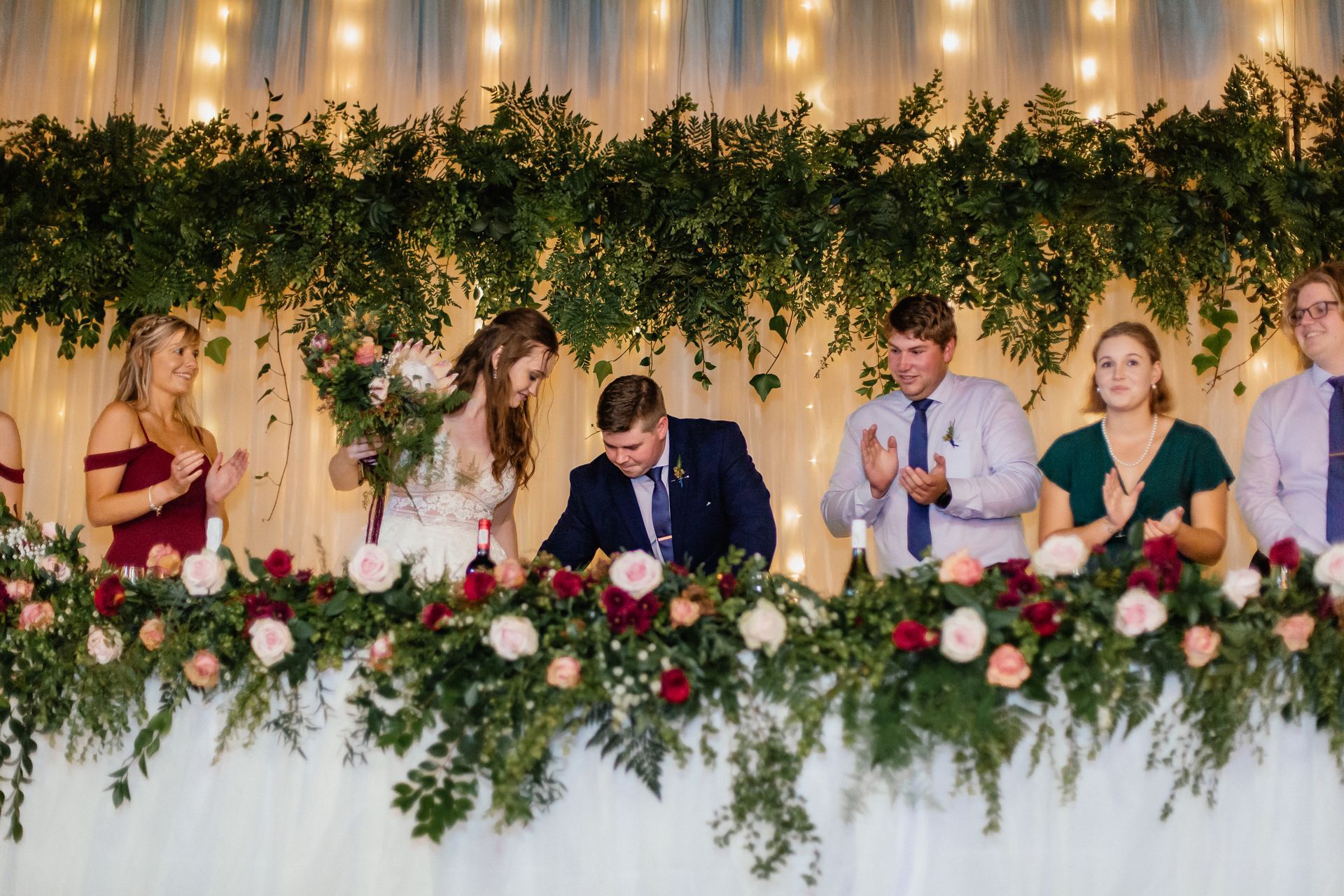 A group of people are sitting at a long table with flowers.