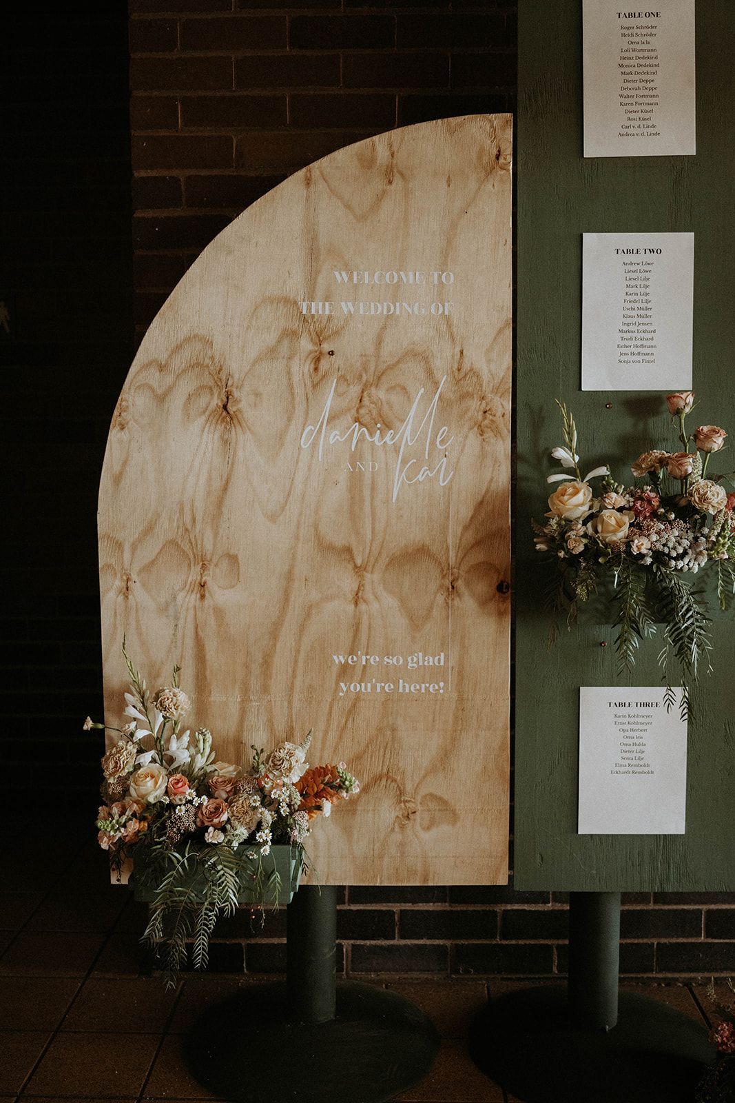 A wooden sign with flowers on it is sitting in front of a brick wall.