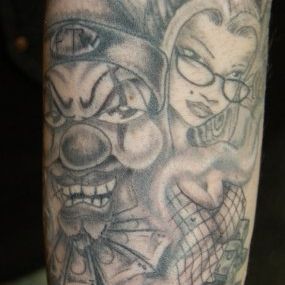 A black and white tattoo of a clown and a woman on a man 's arm.
