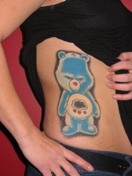 A woman has a blue care bear tattoo on her side
