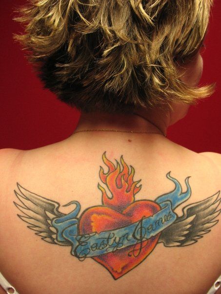 A woman has a tattoo of a heart with flames and wings on her back