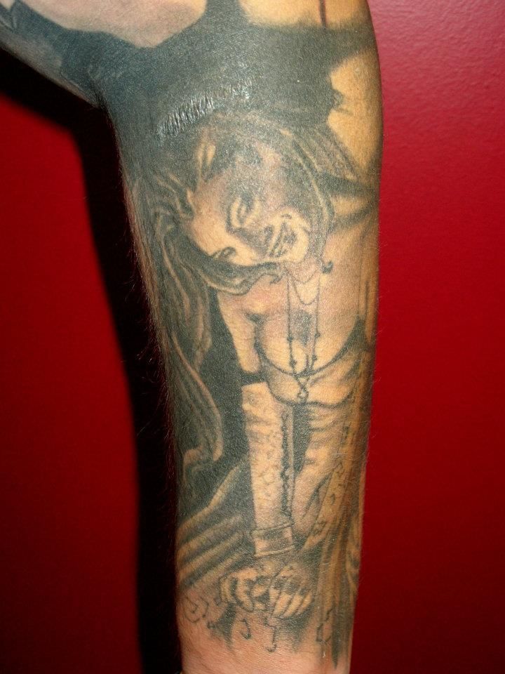 A man has a tattoo of jesus on the cross on his arm.