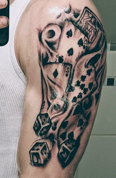 A man has a tattoo of playing cards and dice on his arm.